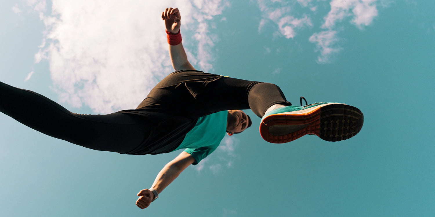 Person in athletic wear performing a jump or flip against a blue sky.