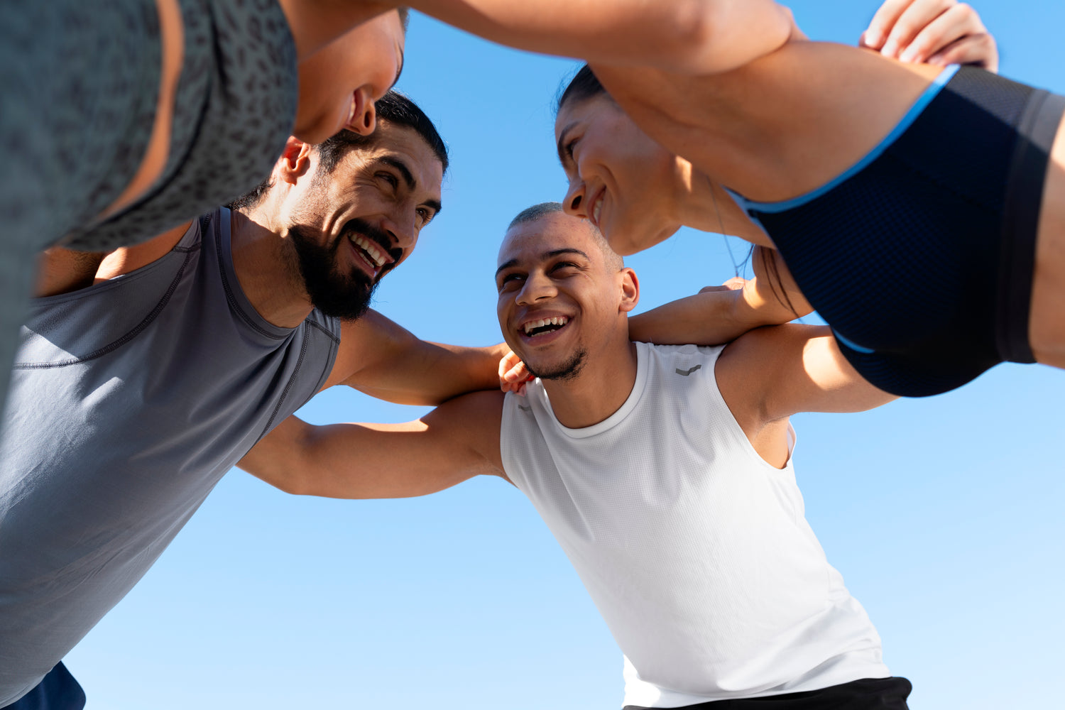 LEAFROG activewear team huddle: Four diverse athletes smiling and showing motivation after a challenging outdoor workout.